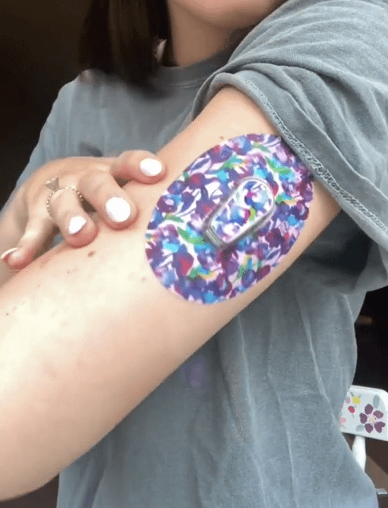 Woman with Vibrant Purple Flowers Dexcom G6 Tape and Transmitter Sticker on arm